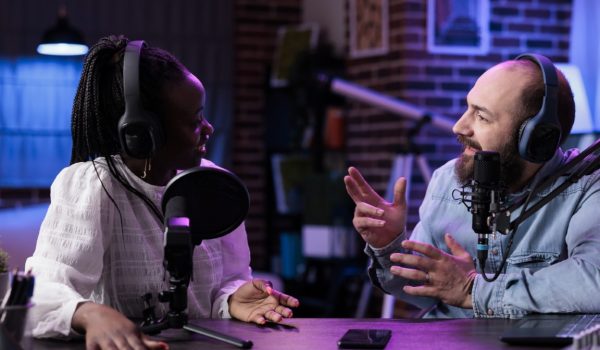 Diverse team of influencers creating channel content on podcast, filming vlog for social media. Modern man and woman recording episode show on camera, live broadcasting conversation.